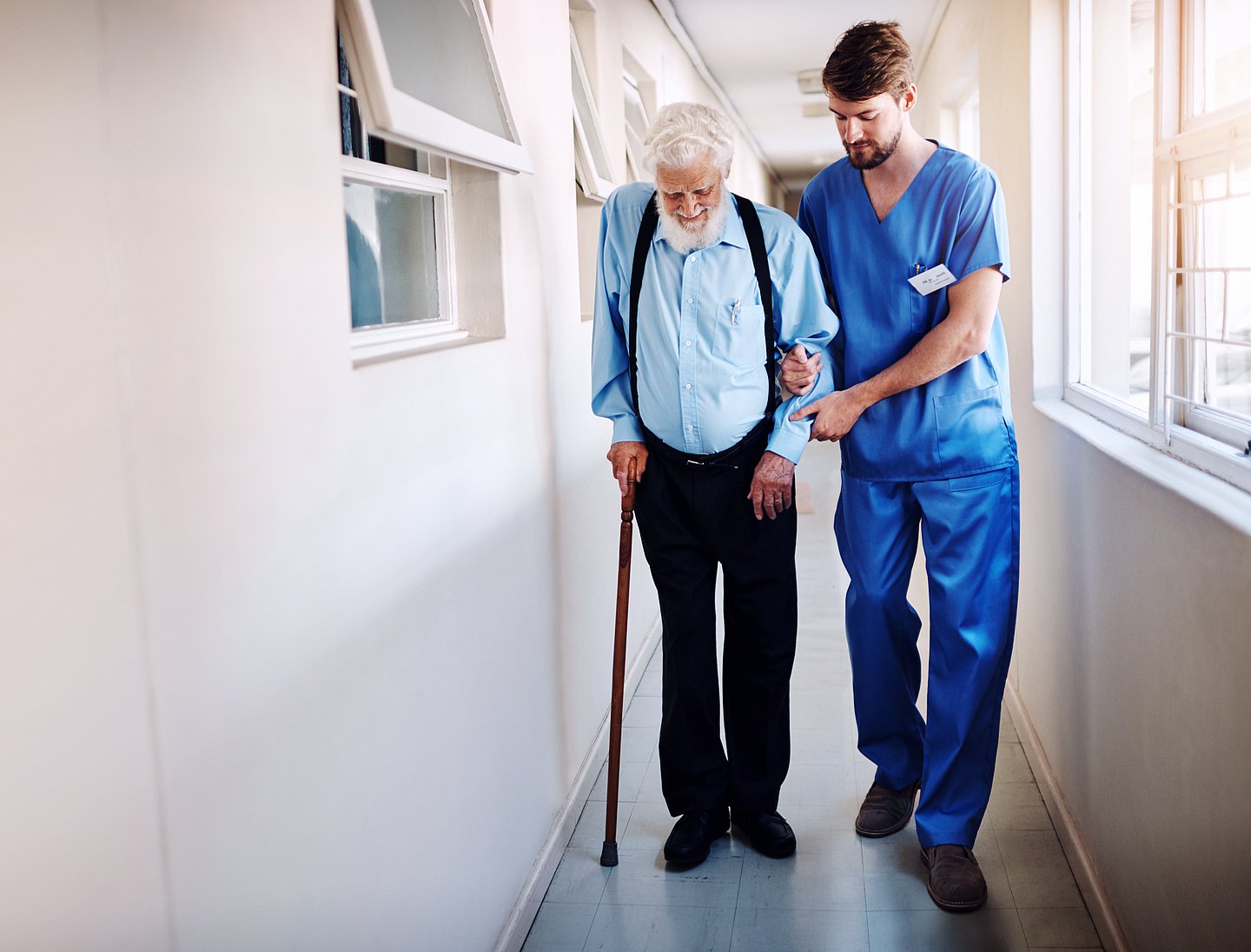 Schmuckbild zeigt eine Pflegekraft, die einen älteren Mann beim Gehen unterstützt.