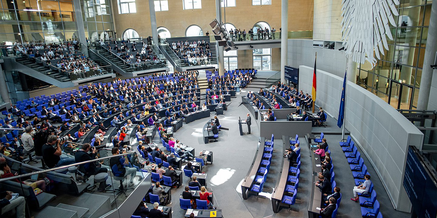 Ds Foto zeigt den vollen Bundestag von der Seite, links die Abgeordneten, rechts die Regierungsbank, das Rednerpult und die Regierungsbänke