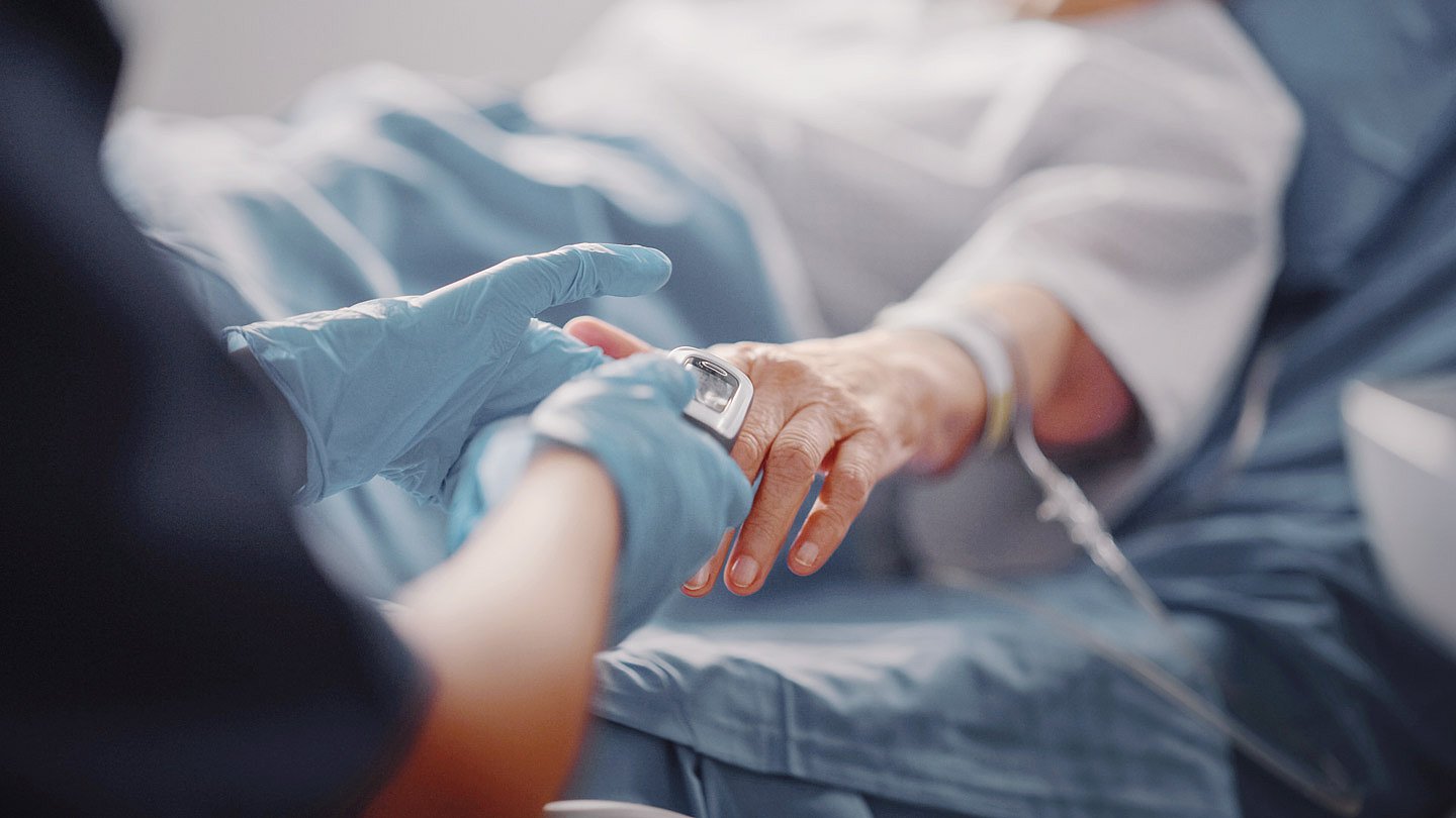 Krankenhaus Foto: Einem bettlägerigen Patienten wird ein Messgerät an den Finger gesteckt.