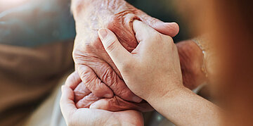 Foto: Nahaufnahme zweier H&auml;nde, die behutsam die Hand einer &auml;lteren Person halten.