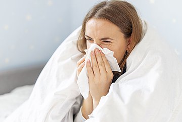 Antibiotika-Verordnungen Westfalen-Lippe Frau liegt krank im Bett, schnupft in ein Taschentuch.