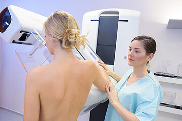 Eine junge Frau steht vor dem Mammographiescreening-Ger&auml;t und wird durch eine Arzthelferin angeleitet.