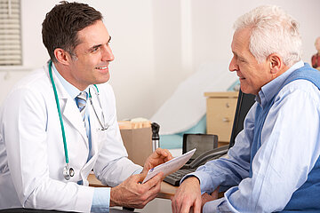 Ein Arzt ist im Gespr&auml;ch mit einem m&auml;nnlichen Patienten. Beide sitzen nah beieinander am Tisch im &auml;rztlichen Sprechzimmer.