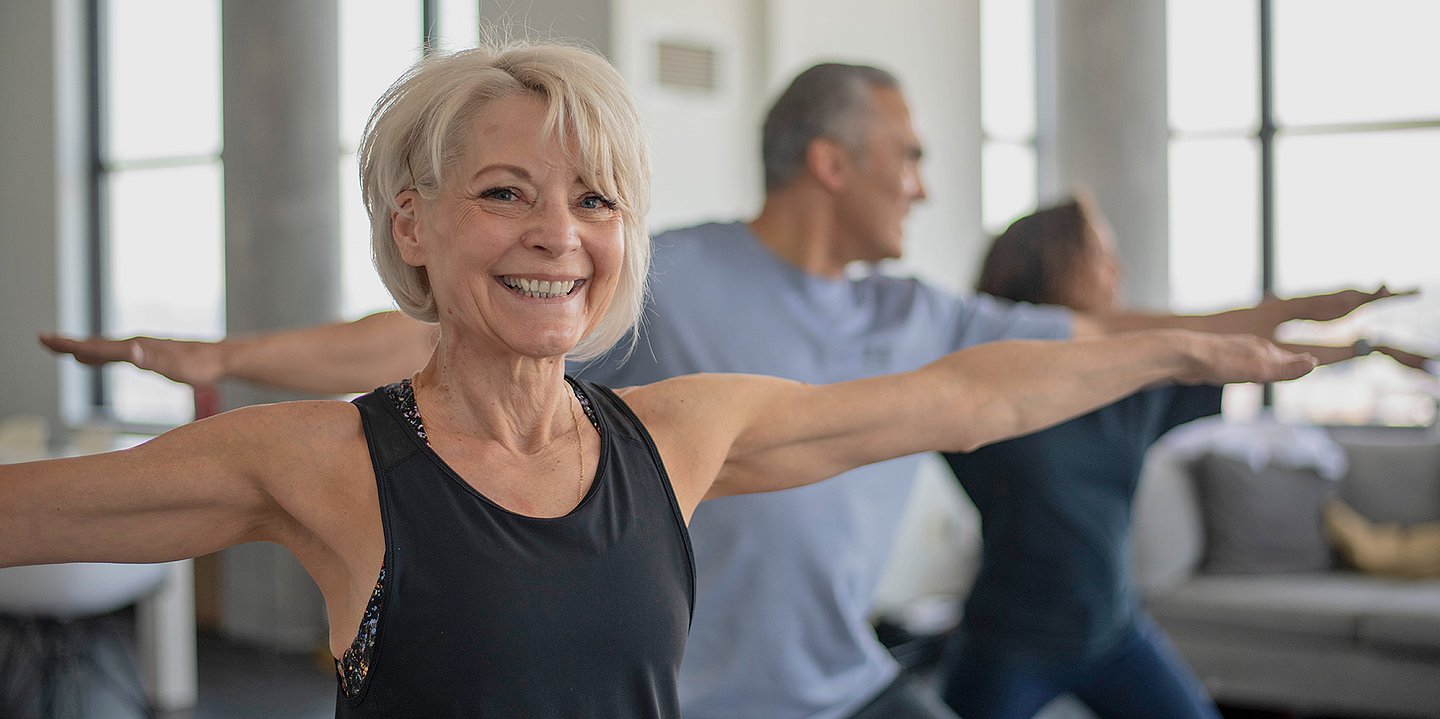 Foto: Ältere Menschen betätigen sich in einer Halle sportlich – vorne im Bild eine Frau, die lächelt.