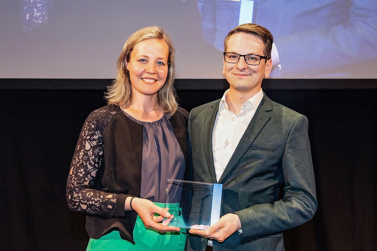 Maxana Baltruweit und Stephan Jaroschek von der AOK Baden-Württemberg halten gemeinsam die Trophäe des Deutschen PR-Preises.