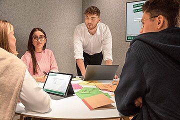 Vier duale Studierende der AOK gruppieren sich an einem Tisch um ein Notebook und tauschen sich aus.