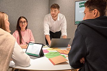 Studierende Vier duale Studierende der AOK gruppieren sich an einem Tisch um ein Notebook und tauschen sich aus.