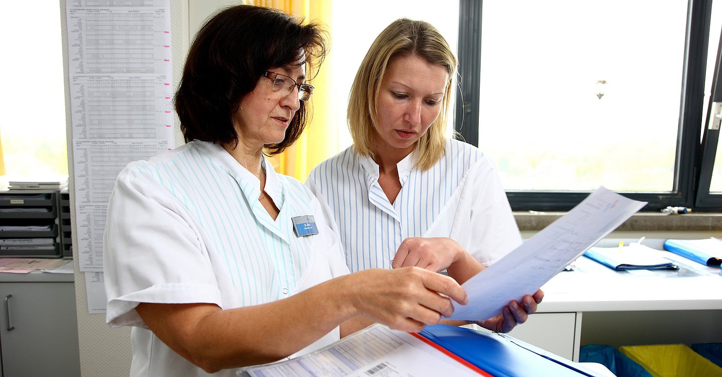Foto: Zwei weibliche Pflegefachkräfte blicken auf einen Dokumentationbogen