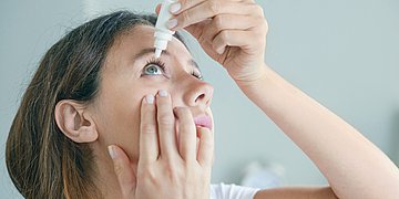 Trockene Augen - Augentropfen Foto: Eine junge Frau tropft sich Augentropfen in ein Auge.