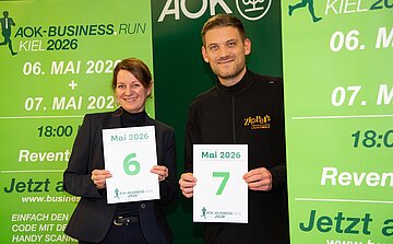 AOK-Landesdirektorin Iris Kröner und Paul Ziplinsky von ZIPPEL´S Läuferwelthalten Kalenderblätter für den 6. und 7. Mai 2026 in den Händen.