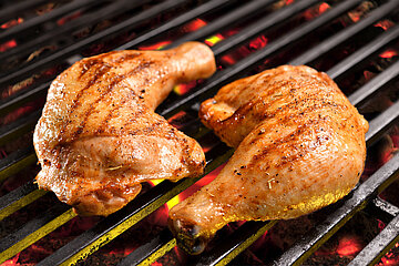 Zwei H&auml;hnchenkeulen liegen auf einem Grillrost, unter dem die gl&uuml;hende Holzkohle zu sehen ist. Die Keulen sind fertig gegrillt, auf der Haut sind die Abdr&uuml;cke des Grillrostes sichtbar.