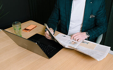 Foto: Professor Dr. David Matusiewicz mit Laptop vor sich und Zeitung in der Hand.