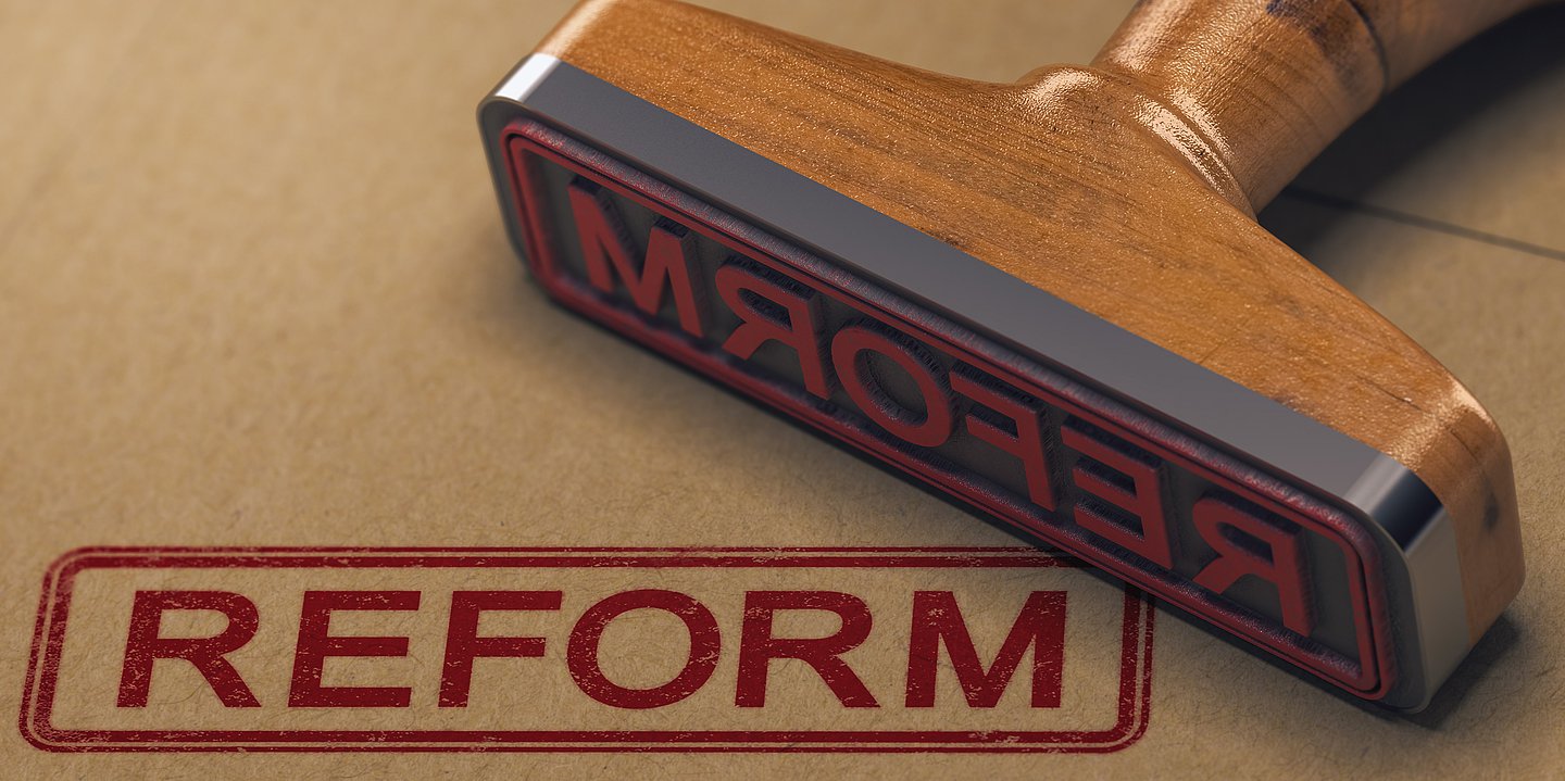 Ein Stempel mit dem Begriff "Reform" liegt auf einem Tisch, daneben ist der Begriff "Reform" gestempelt.