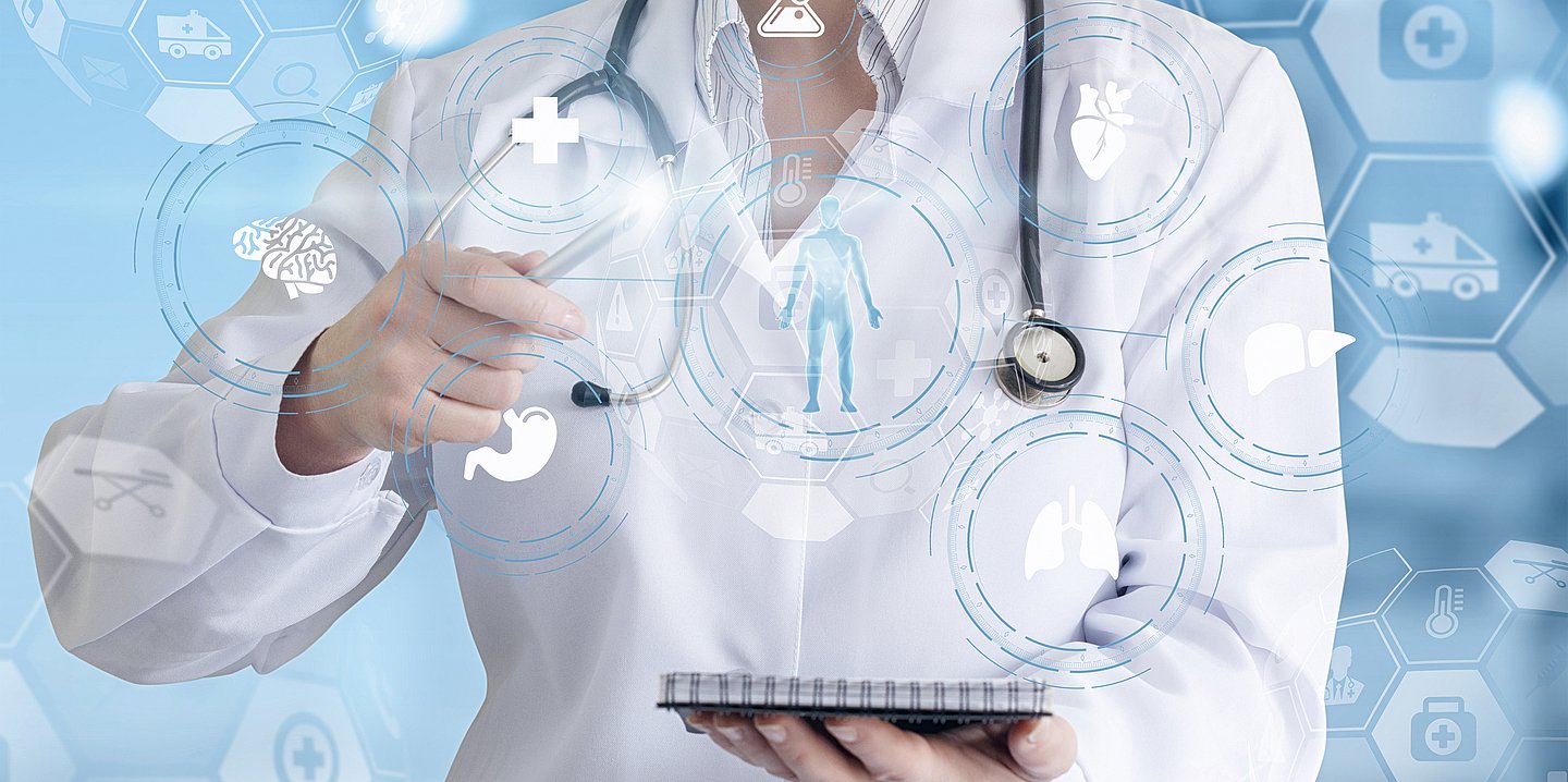 Symbolbild einer Ärztin im weißen Kittel. Sie hält einen Block in der linken Hand. Mit der rechten bedient sie vor sich ein digitales Panel mit verschiedenen medizinischen Symbolen, die um die Silhouette eines Patienten kreisen.