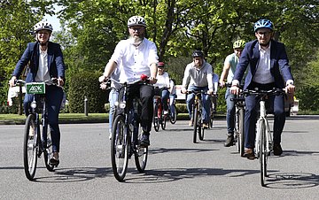 Foto zeigt eine Gruppe Menschen, die mit dem Fahrrad fahren. Vorneweg die AOK-Landesdirektorin Iris Kr&ouml;ner, Landes-Verkehrsminister Claus Ruhe Madsen und Hako-Gesch&auml;ftsf&uuml;hrer Blache. Es folgen dahinter weitere Mitarbeiter der Firma Hako.