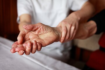 Eine Pflegekraft h&auml;lt die Hand einer &auml;lteren Dame.