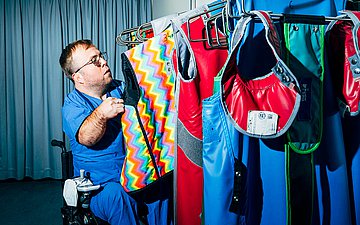 Foto von Charité-Arzt Dr. Leopold Rupp, wie er einen bunten Röntgenkittel an einer Stange auswählt