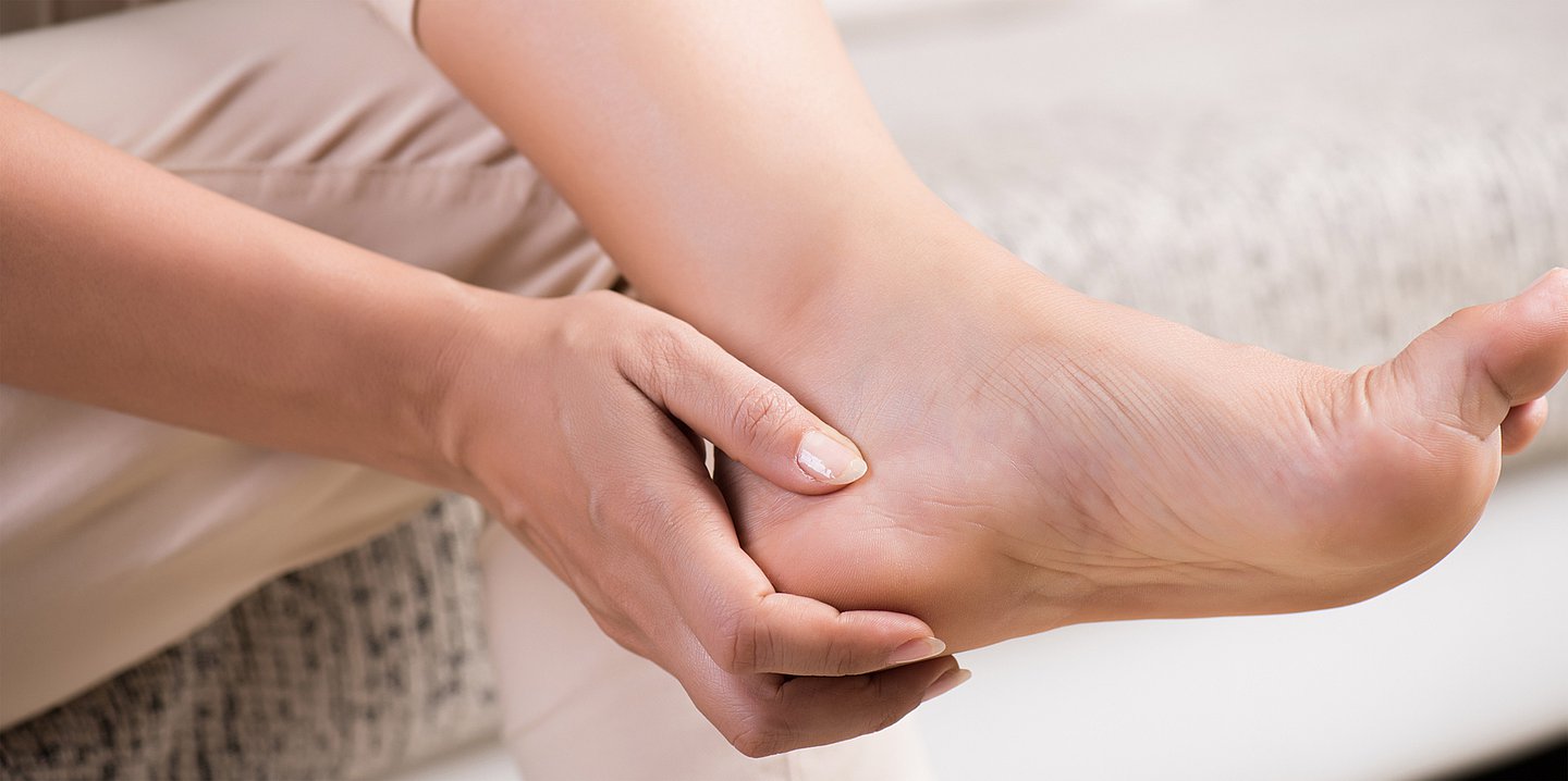 Foto: Eine Frau fasst sich mit der Hand an ihre Ferse.