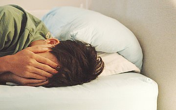 Chronische Erschöpfung Ein junger Mann liegt erschöpft im Bett.