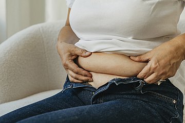 Adipositas Eine Person mit Gewichtsproblemen betastet ihren Speckgürtel.