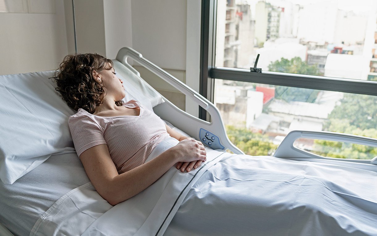 Foto einer Frau, die in einem Klinikbett liegt und aus dem Fenster blickt