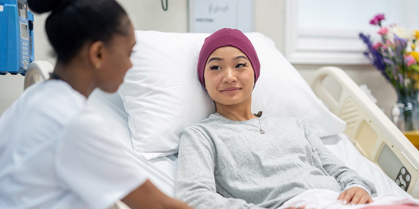 Eine Krebspatientin liegt im Krankenhausbett und eine Ärztin hält ihre Hand.
