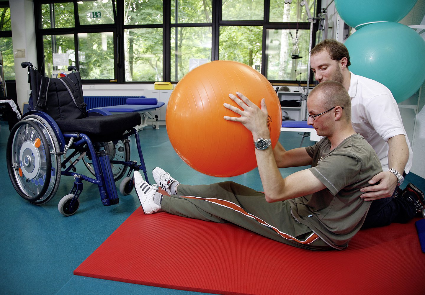 Eine Pflegekraft hilft einem Patienten bei Übungen mit dem Gymnastikball.