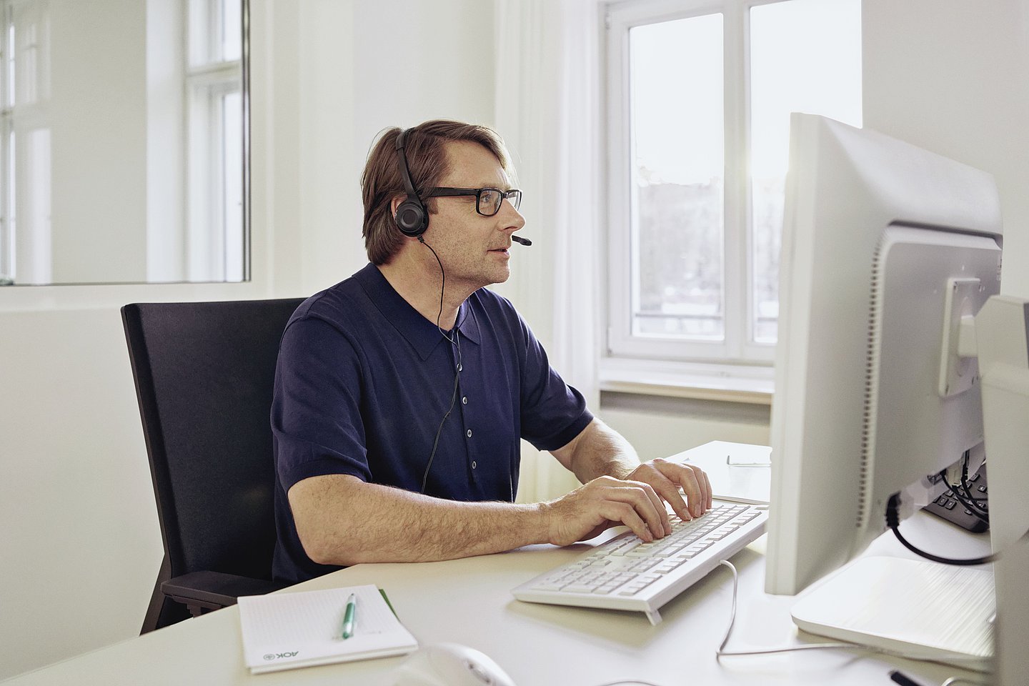 Foto: ein Mann sitzt mit einem Headset in einem Büro vor einem Bildschirm 