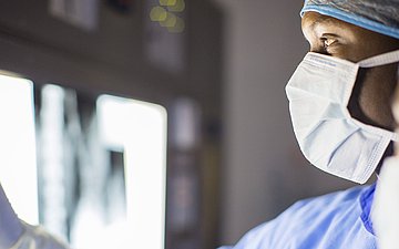 OP-Team bei Röntgen-Diagnose Zwei Ärzte mit OP-Haube und Mundschutz (rechts, Köpfe im Anschniitt) schauen auf ein Rötgenbild, dass an einen Scheinwerfer geklemmt ist.