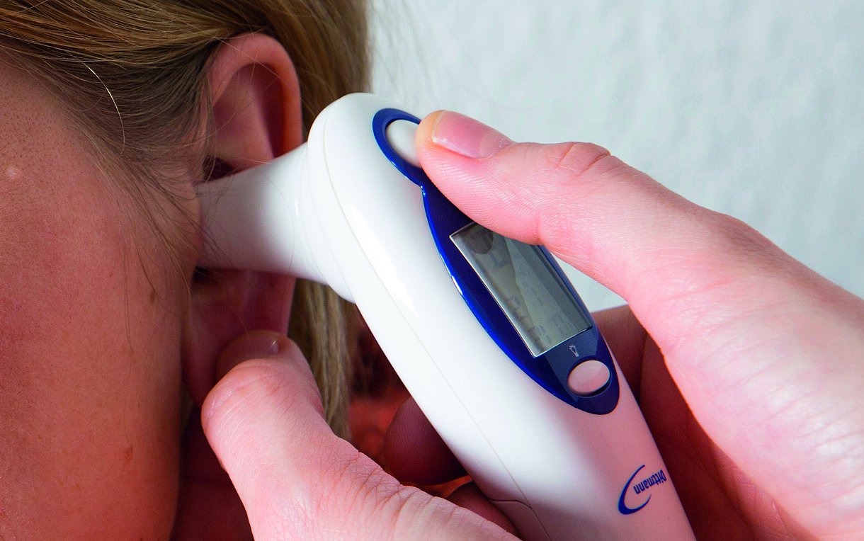 Foto: Bei einer jungen Frau wird das Fieber mit einem Ohrthermometer gemessen.