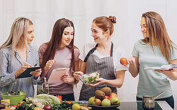 Vier junge Frauen bereiten gemeinsam Fr&uuml;chte und Salate zu. 