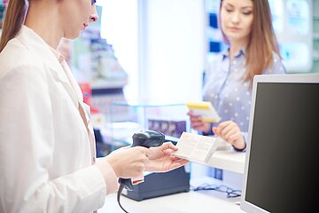 Das Bild zeigt eine Apothekerin, die f&uuml;r eine Kundin ein Medikament einscannt.