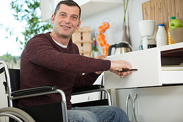 Ein Mann im Rollstuhl &ouml;ffnet eine Schublade in der K&uuml;chenzeile (s)einer K&uuml;che.