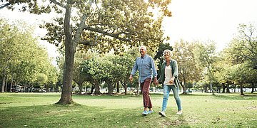 Bewegung In einem grünen Park geht ein älteres Ehepaar spazieren.