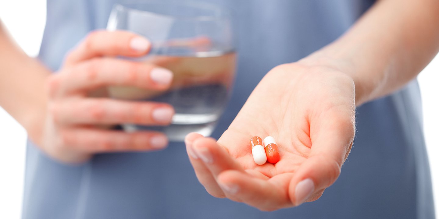 Foto: Eine Pflegekraft hält in einer Hand ein Glas Wasser und in der anderen Hand Medikamente.