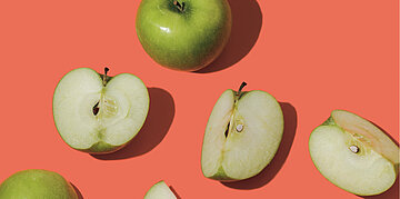 Foto: Aufgeschnittene gr&uuml;ne &Auml;pfel auf rotem Hintergrund.