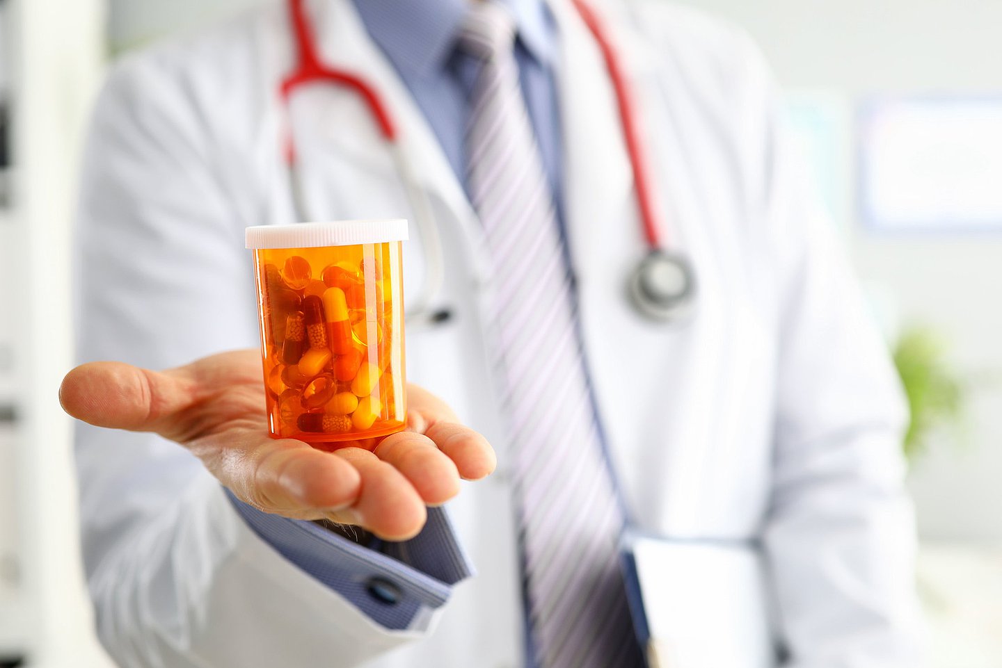 Foto zeigt einen Arzt oder eine Ärztin, die in der ausgestreckten Hand ein Behältnis mit Tabletten zeigt.