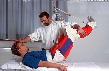 Ein Physiotherapeut behandelt einen Patienten am Schlingentisch.