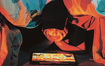 Mediensucht Kinder Foto eines Jungen, der heimlich unter der Decke aufs iPad schaut