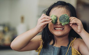 Ernährung Foto: Ein Kind hält sich Brokkoli-Röschen vor die Augen.