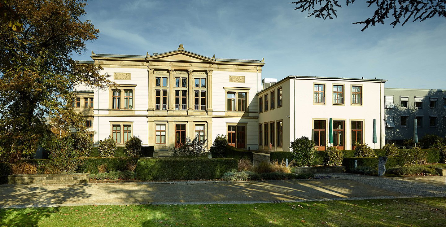 Das Foto zeigt das Gebäude des Landtags des Saarlandes. Ein weißes, klassisistisch anmutendes Gebäude mitkleiner Grünanlage im Vordergrund 