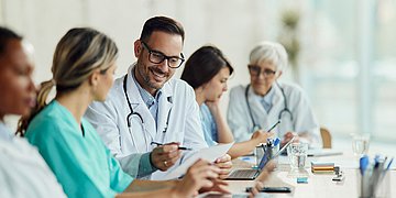 Selbstverwaltung Verschiedene Ärzte und Krankenschwestern sitzen am Tisch und diskutieren ein Thema.