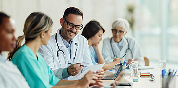 Verschiedene &Auml;rzte und Krankenschwestern sitzen am Tisch und diskutieren ein Thema.