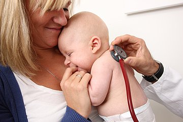 Eine Mutter hält ihr Baby in ihrem Arm. Eine medizinische Fachperson hört ein Baby mit einem Stethoskop ab. 