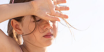 Ein Kleinkind h&auml;lt die Hand vor die Augen vor der Sonne und schwitzt.