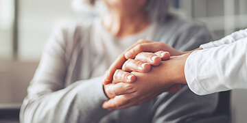 Zwei Frauen halten sich an den H&auml;nden. Die Hand ist im Vordergrund und nur der eine Oberk&ouml;rper im Hintergrund erkennbar. Von der zweiten Frau sieht man nur die Arme.