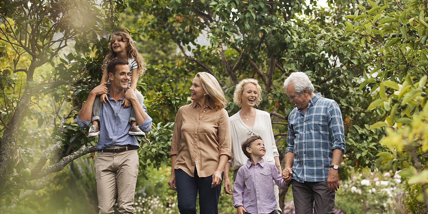 Eine Familie mit Kindern, Eltern und Großeltern geht in der Natur spazieren. 