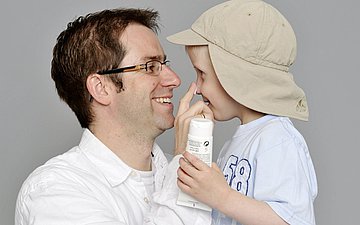 Sonnenschutz Symbolbild für Sonnenschutz zeigt einen Vater, der seinem Kind die Nase eincremt