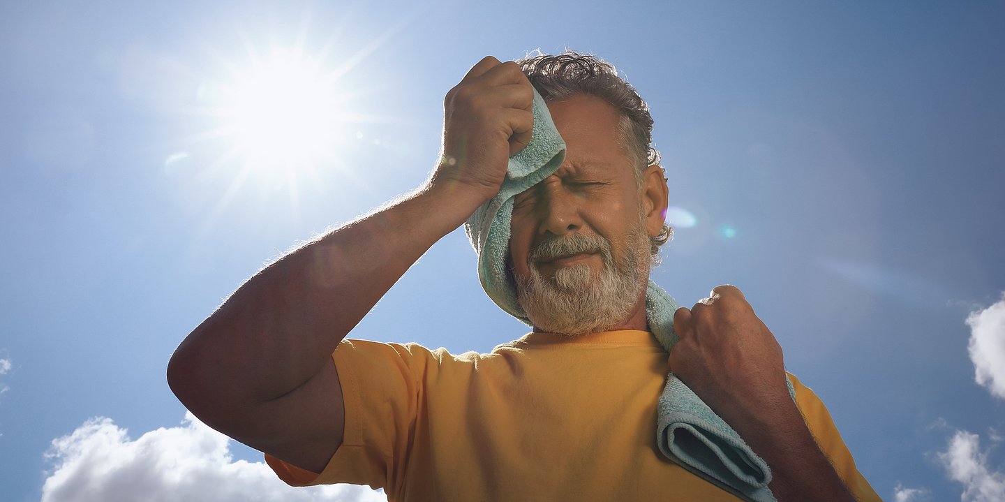 Foto: Mann steht in der Sonne und trocknet sich den Schweiß von der Stirn ab
