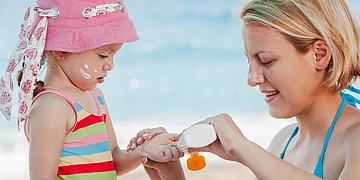 Foto: Eine junge Mutter cremt ihr Kind am Strand mit Sonnencreme ein.